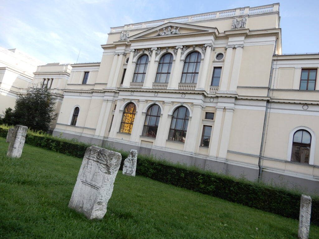 Små stećci foran Nationalmuseet i Sarajevo. Det ikoniske Holiday Inn-hotel spejles i museets vindue. Herfra blev Suada Dilberović og Olga Sučić snigmyrdet under etnisk blandede antikrigsprotester den 5. april 1992. (Jimmy Munk Larsen)